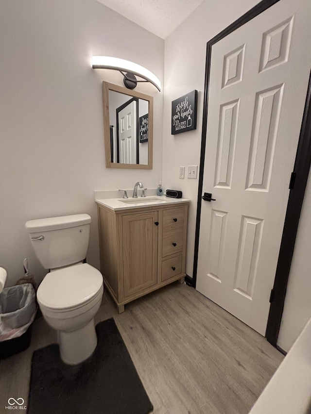 half bathroom with vanity, toilet, and wood finished floors
