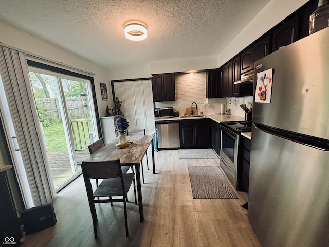 kitchen featuring light wood finished floors, a sink, under cabinet range hood, light countertops, and appliances with stainless steel finishes
