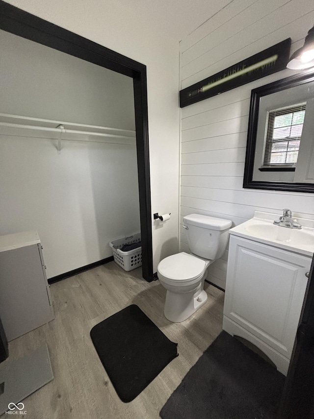 bathroom with toilet, wooden walls, wood finished floors, and vanity