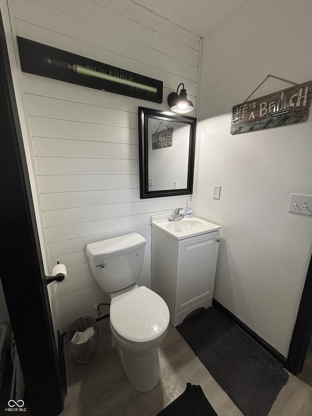 half bath with toilet, wood walls, wood finished floors, and vanity