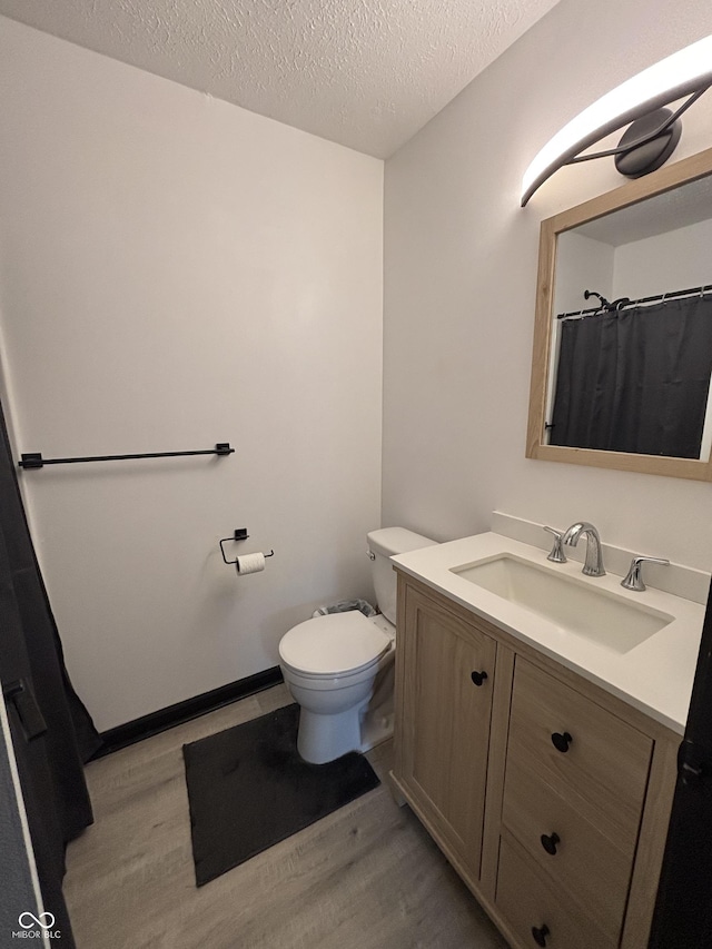 bathroom with toilet, vanity, a textured ceiling, and wood finished floors