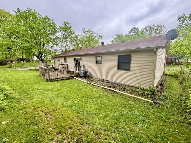 rear view of property with central AC unit, a wooden deck, fence, and a lawn