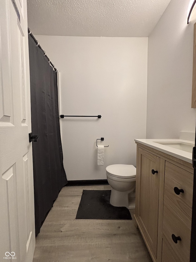bathroom with vanity, toilet, a textured ceiling, and wood finished floors