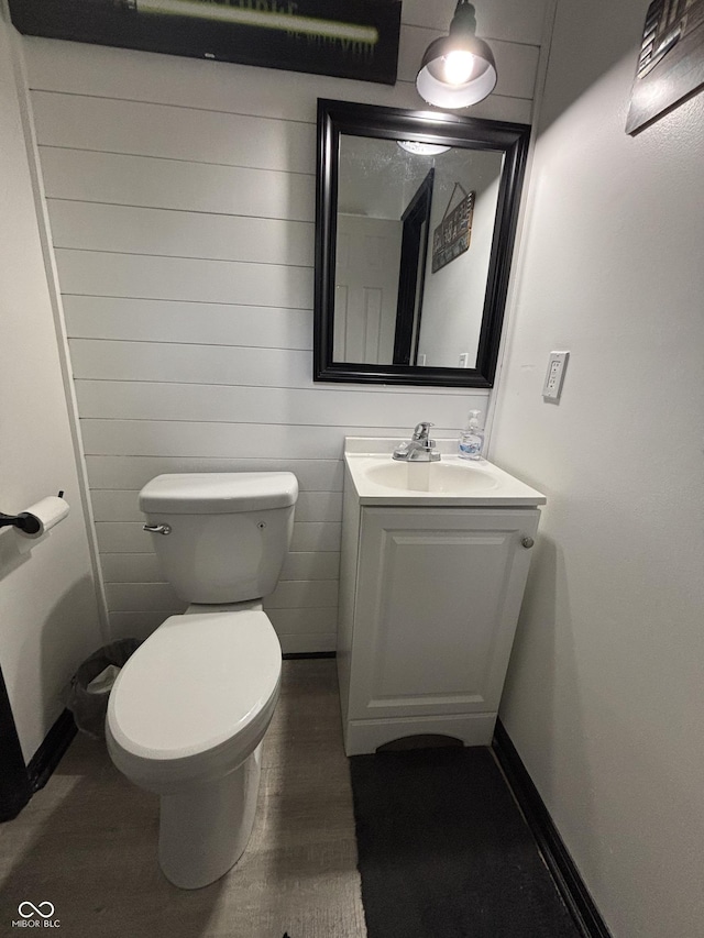 half bathroom featuring toilet, baseboards, and vanity