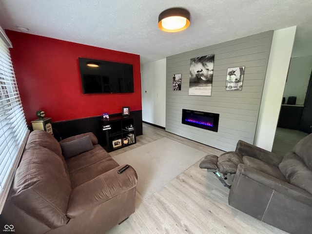 living room featuring a textured ceiling, wood finished floors, a fireplace, and an accent wall