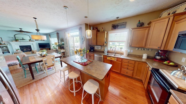 18247 Kinder Oak Dr, Noblesville, IN 46062 - kitchen with a sink, a textured ceiling, stainless steel appliances, a glass covered fireplace, and light wood finished floors
