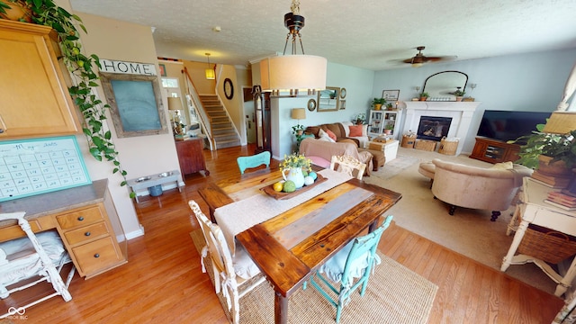 18247 Kinder Oak Dr, Noblesville, IN 46062 - dining area featuring a ceiling fan, light wood-style flooring, stairway, a textured ceiling, and a glass covered fireplace