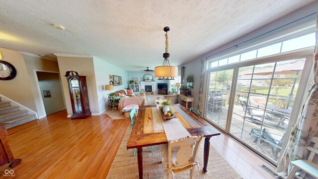 18247 Kinder Oak Dr, Noblesville, IN 46062 - dining area with light wood-type flooring, a textured ceiling, a fireplace, baseboards, and stairs