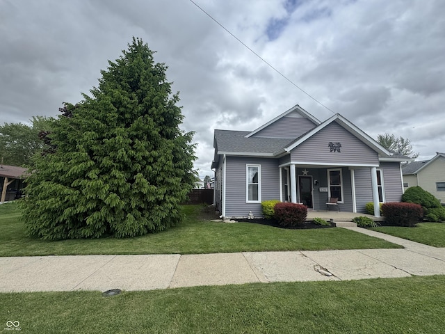 bungalow-style home featuring a porch, a front lawn, and roof with shingles