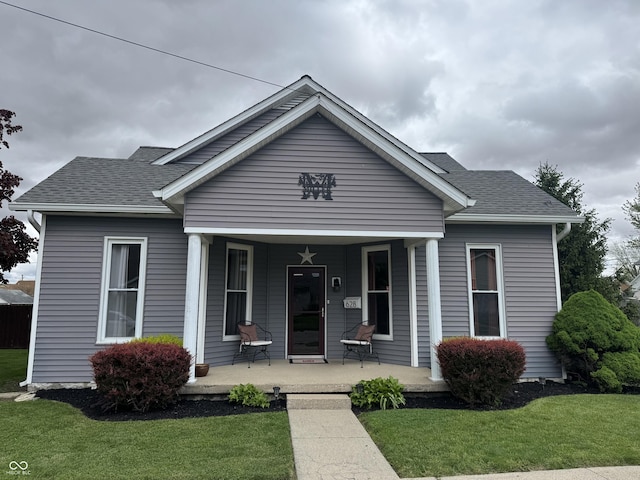 bungalow-style house featuring covered porch, a front yard, and roof with shingles