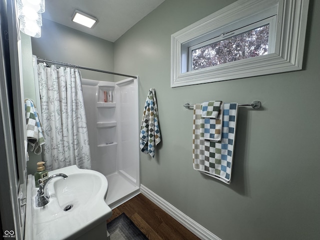 bathroom with a shower with curtain, wood finished floors, baseboards, and a sink