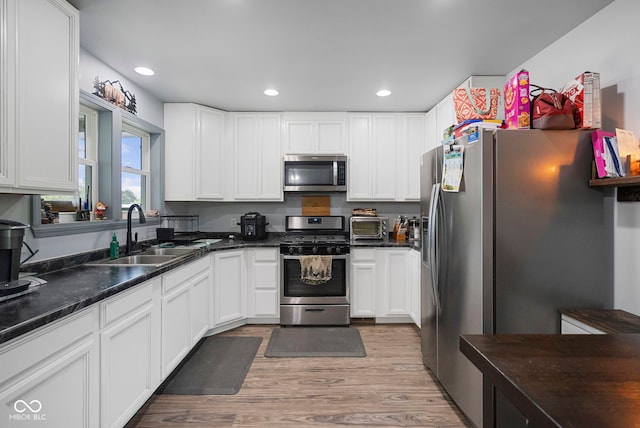 kitchen featuring a sink, a toaster, light wood-style flooring, white cabinets, and appliances with stainless steel finishes