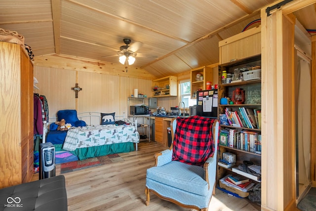 bedroom with a sink, lofted ceiling, light wood-style flooring, and wooden walls