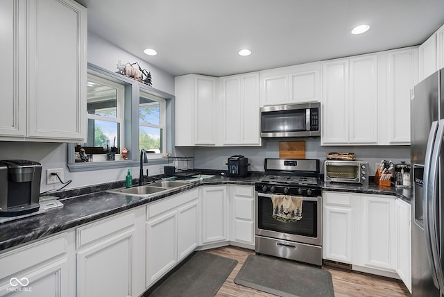 kitchen featuring white cabinetry, light wood-style floors, appliances with stainless steel finishes, and a sink