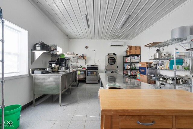 kitchen featuring baseboards, a wall mounted AC, and stainless steel electric stove