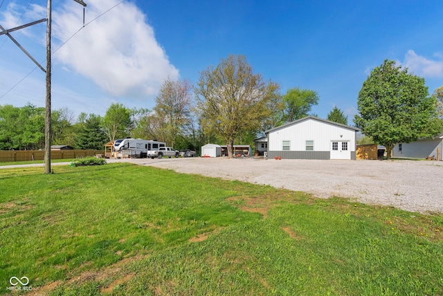 view of front of home featuring fence, driveway, a shed, a front yard, and an outbuilding