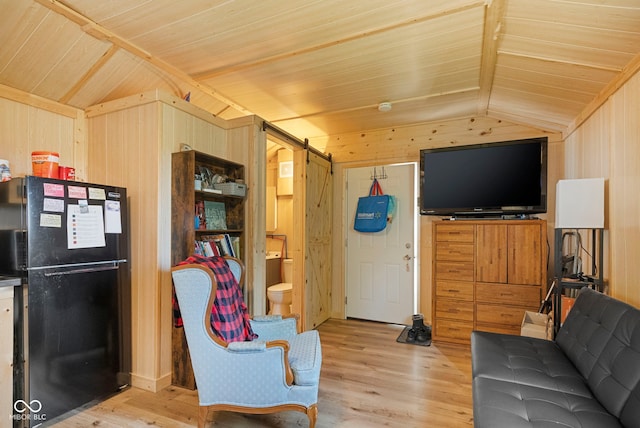 living room with lofted ceiling, wood walls, a barn door, and light wood-style floors