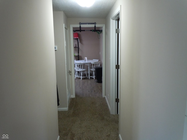 corridor featuring a textured ceiling, carpet, and baseboards