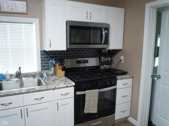 kitchen with a sink, backsplash, light countertops, white cabinets, and appliances with stainless steel finishes