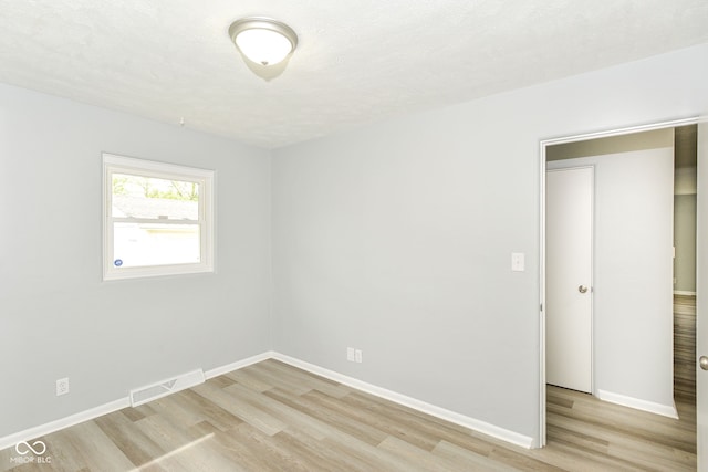 spare room with light wood-type flooring, visible vents, and baseboards