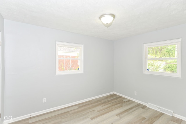 unfurnished room with light wood-style floors, visible vents, baseboards, and a healthy amount of sunlight