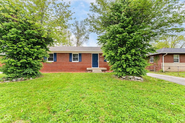 ranch-style house featuring brick siding, fence, entry steps, a front yard, and aphalt driveway
