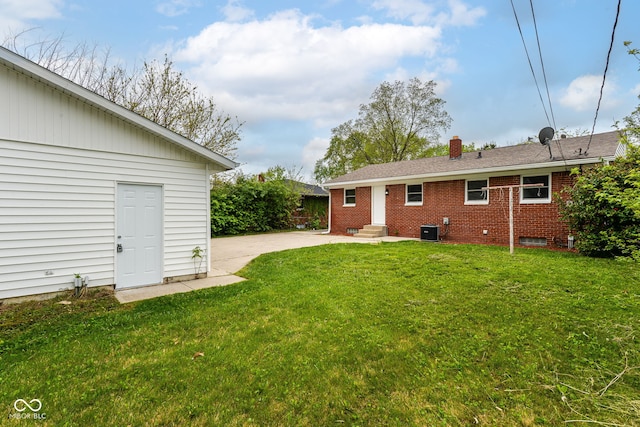 rear view of house featuring brick siding, entry steps, cooling unit, a chimney, and a lawn
