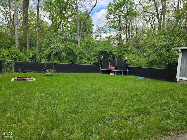view of yard featuring an outdoor fire pit, a trampoline, and fence