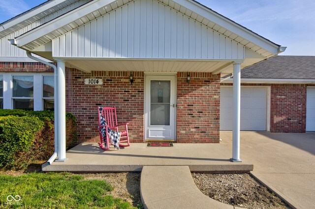 entrance to property featuring brick siding, an attached garage, driveway, and covered porch