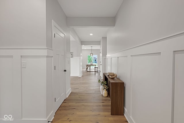 hallway featuring wainscoting, a decorative wall, and light wood-type flooring