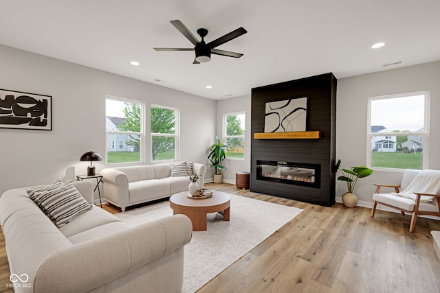 living room featuring light wood-style flooring, baseboards, ceiling fan, a large fireplace, and recessed lighting