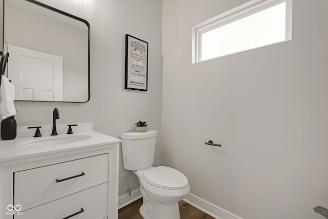 half bathroom with vanity, toilet, baseboards, and wood finished floors