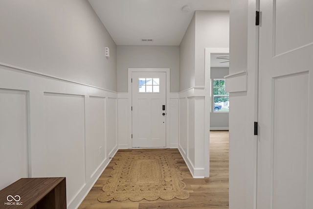entryway featuring light wood-type flooring, visible vents, a decorative wall, and wainscoting