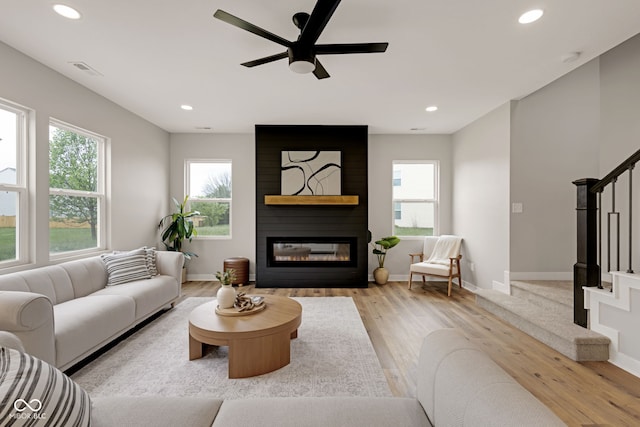 living area with stairway, a fireplace, light wood-type flooring, and plenty of natural light