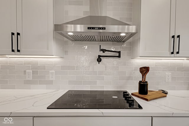 kitchen with wall chimney range hood, black electric stovetop, decorative backsplash, and white cabinets