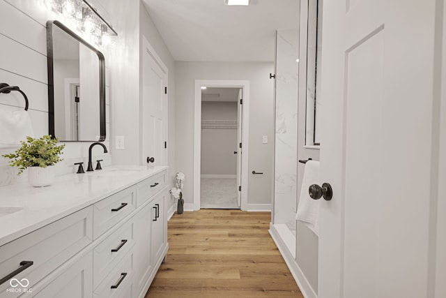 bathroom featuring double vanity, a marble finish shower, wood finished floors, a sink, and a spacious closet
