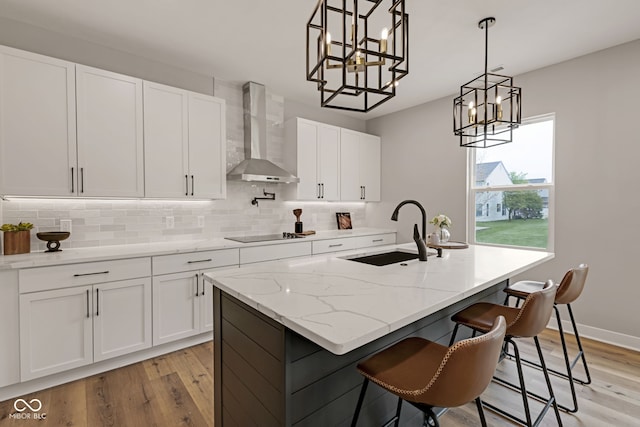 kitchen featuring a sink, backsplash, a notable chandelier, and wall chimney exhaust hood