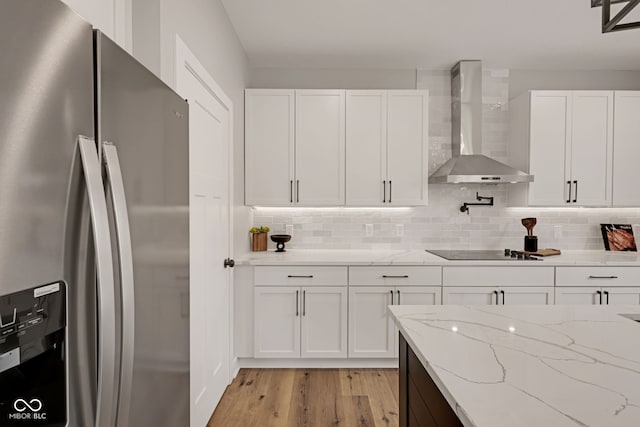 kitchen featuring freestanding refrigerator, white cabinetry, black electric stovetop, and wall chimney exhaust hood
