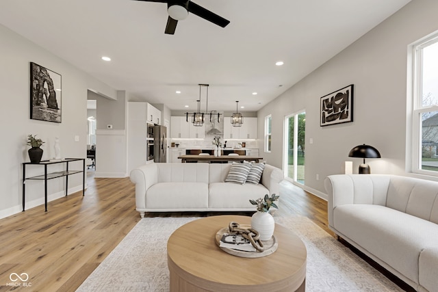 living area with light wood finished floors, ceiling fan with notable chandelier, plenty of natural light, and recessed lighting
