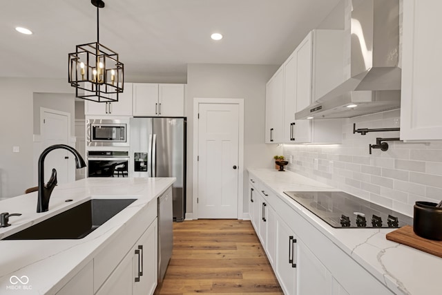 kitchen with a sink, stainless steel appliances, wall chimney range hood, light wood-style flooring, and white cabinets