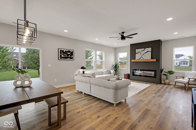 living room featuring light wood-style flooring, recessed lighting, baseboards, ceiling fan, and a large fireplace