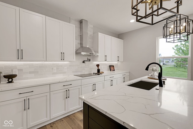 kitchen featuring black electric cooktop, wall chimney exhaust hood, decorative backsplash, and a sink