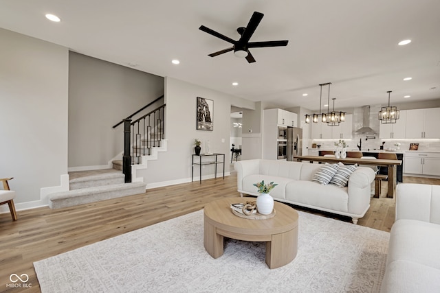 living area with ceiling fan with notable chandelier, recessed lighting, stairway, light wood-style flooring, and baseboards