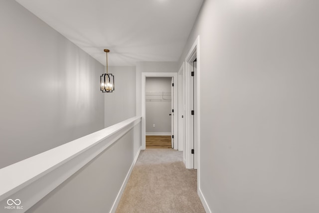 hallway with baseboards, a notable chandelier, and light carpet