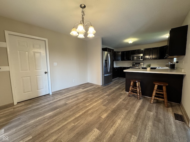 2725 Falcon Ct, Seymour, IN 47274 - kitchen with appliances with stainless steel finishes, dark cabinetry, wood finished floors, a chandelier, and a peninsula