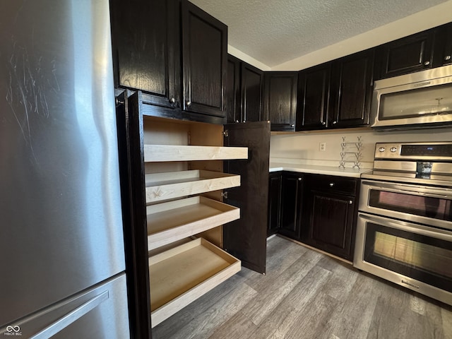 2725 Falcon Ct, Seymour, IN 47274 - kitchen featuring stainless steel appliances, dark cabinetry, light wood-type flooring, light countertops, and a textured ceiling
