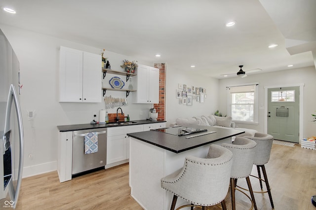 kitchen with stainless steel appliances, a sink, open shelves, a breakfast bar, and light wood finished floors