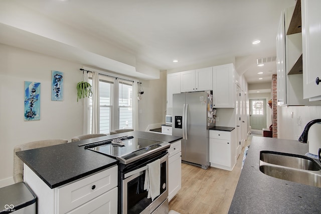 kitchen featuring stainless steel appliances, a sink, dark countertops, a kitchen island, and light wood-type flooring