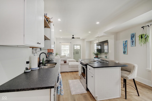 kitchen with stainless steel range with electric stovetop, a sink, a breakfast bar area, dark countertops, and white cabinets