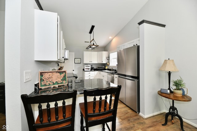 kitchen with a peninsula, wood finished floors, vaulted ceiling, white cabinetry, and appliances with stainless steel finishes